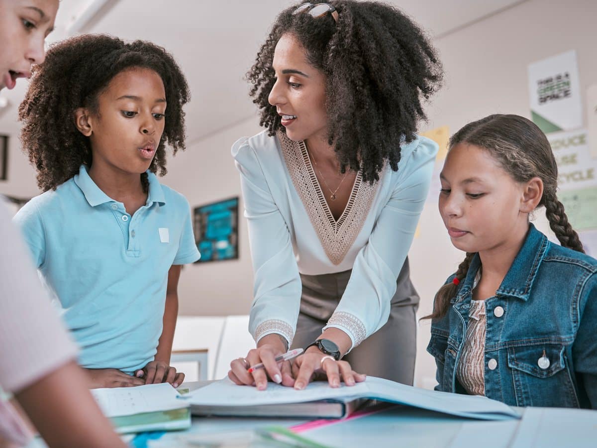 A teacher leaning over a desk, working through a question with a group of students